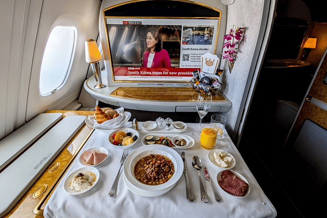 A fully laid-out dining service and personal touchscreen monitor showing a news broadcast for a private first class suite.
